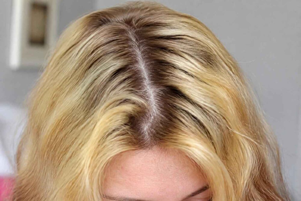 Blond włosy z ciemniejszym odrostem i przedziałkiem Zbliżenie blond włosów z wyraźnym ciemniejszym odrostem i przedziałkiem na środku głowy