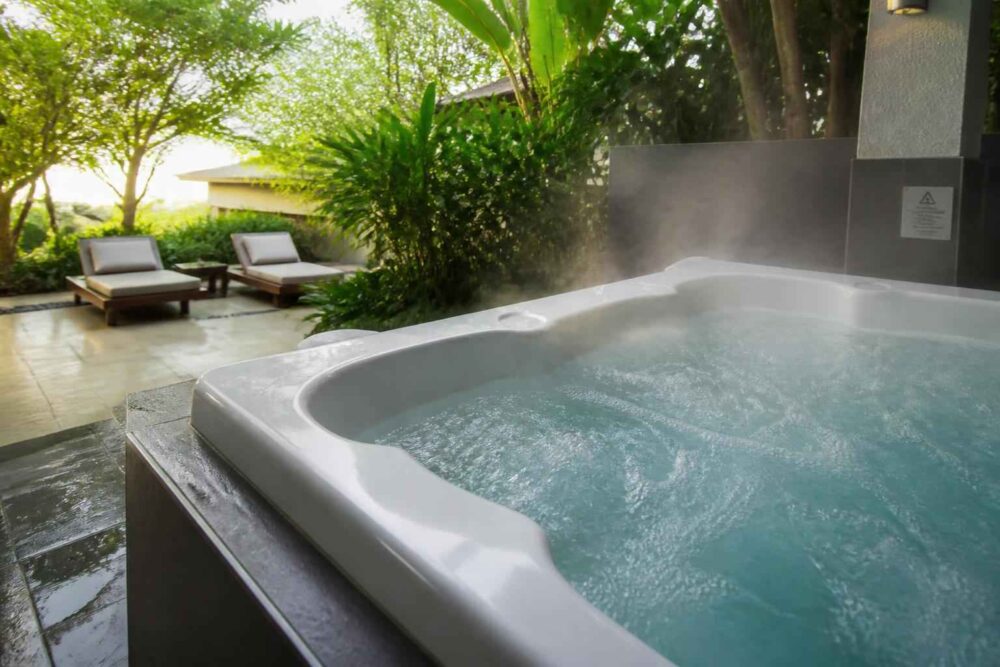 Wanna spa z parującą wodą na tarasie, obok leżaków i bujnej roślinności tropikalnej
