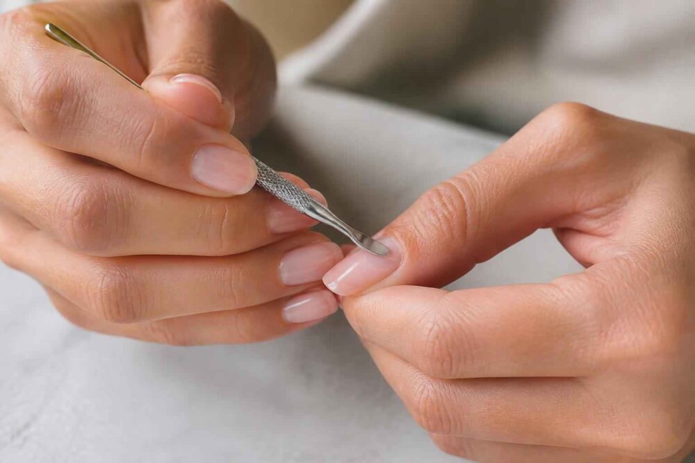 Dłonie podczas odsuwania skórek metalowym kopytkiem do manicure